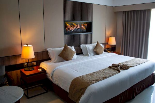 A neatly arranged hotel room features a large bed, side tables with lamps, a decorative headboard, and a curtain-draped window.