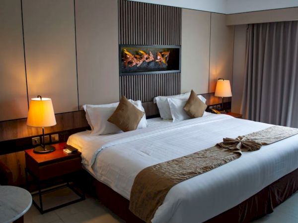 A neatly arranged hotel room features a large bed, side tables with lamps, a decorative headboard, and a curtain-draped window.