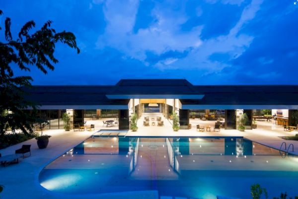 A luxurious outdoor pool area at night, with a modern building and lounge seating, creates a serene and inviting atmosphere.