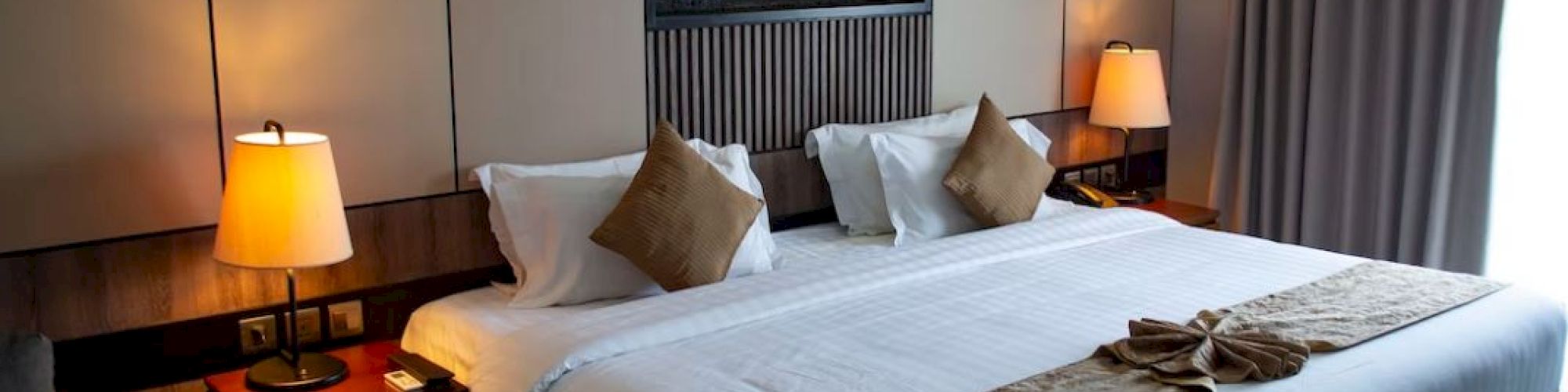 A cozy hotel room with a large bed, decorative pillows, bedside lamps, and a modern wall design behind the headboard.