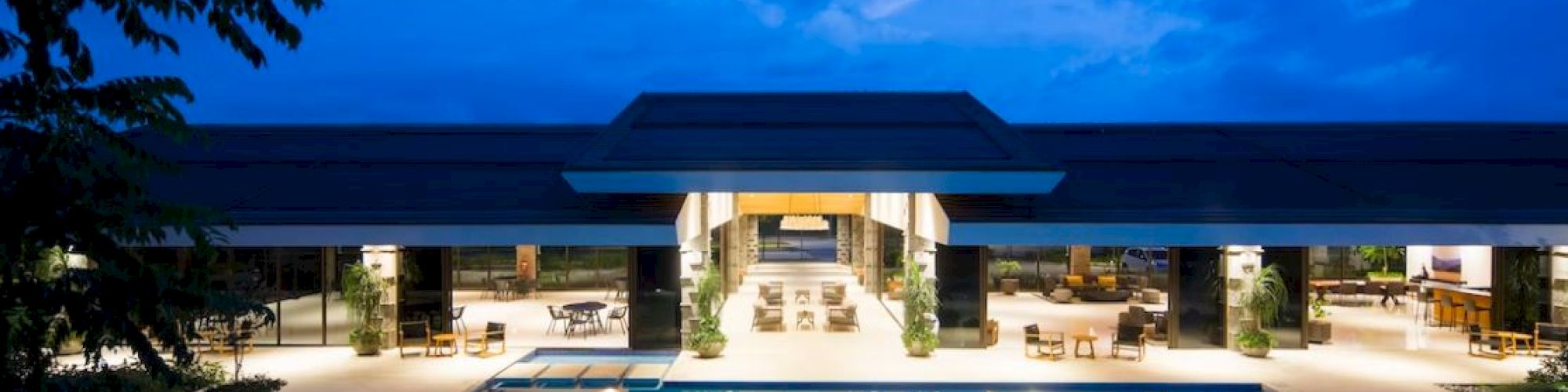 A luxurious poolside view at night with an illuminated modern building and lounge areas, set against a partly cloudy night sky.