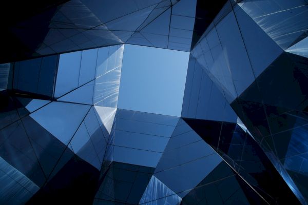 The image shows a view of glass skyscrapers from below, creating a geometric pattern with a clear blue sky at the center.