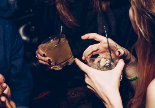 People are enjoying drinks and conversation at a social gathering, with focus on their hands and beverages.