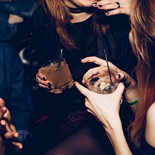 People are enjoying drinks and conversation at a social gathering, with focus on their hands and beverages.