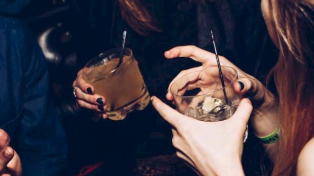 People are enjoying drinks and conversation at a social gathering, with focus on their hands and beverages.