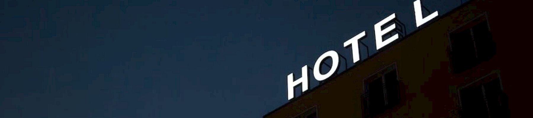 A hotel building at night with an illuminated "HOTEL" sign on the roof, missing one letter.
