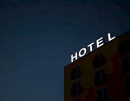 A hotel building at night with an illuminated "HOTEL" sign on the roof, missing one letter.