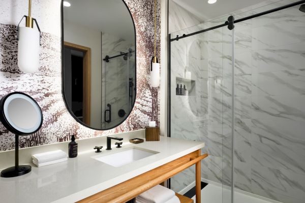 Modern bathroom with a large oval mirror, sleek sink, marble shower, and stylish lighting. Neatly arranged towels complete the look.