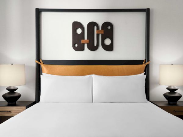 A neatly made bed with white linens, flanked by two lamps on side tables, and geometric artwork above the headboard.
