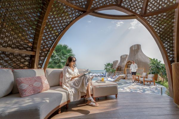 A woman reads in a stylish outdoor lounge with a sea view. Elegant structures and tropical plants create a serene atmosphere.