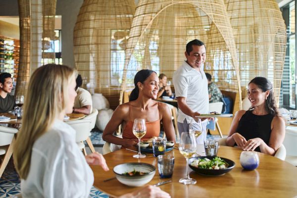 People enjoying a meal at a stylish restaurant with wicker decor and natural lighting.