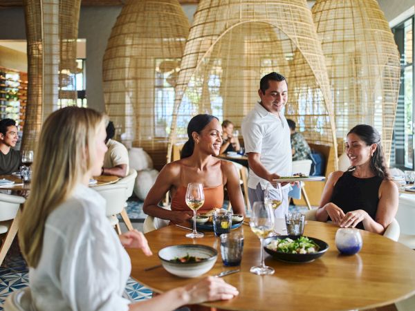 People enjoying a meal at a stylish restaurant with wicker decor and natural lighting.