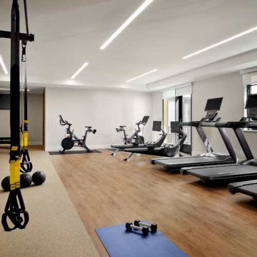 A modern gym with treadmills, bikes, weights, and mats inside a bright, spacious room.