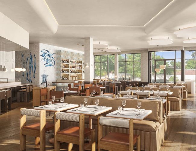 A modern, spacious restaurant with wooden tables, chairs, and a long bar counter, decorated with plants and large windows letting in natural light.