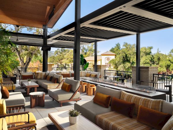 A stylish outdoor lounge on a shaded terrace with wooden furniture, neutral cushions, and potted plants, ideal for relaxation and socializing.