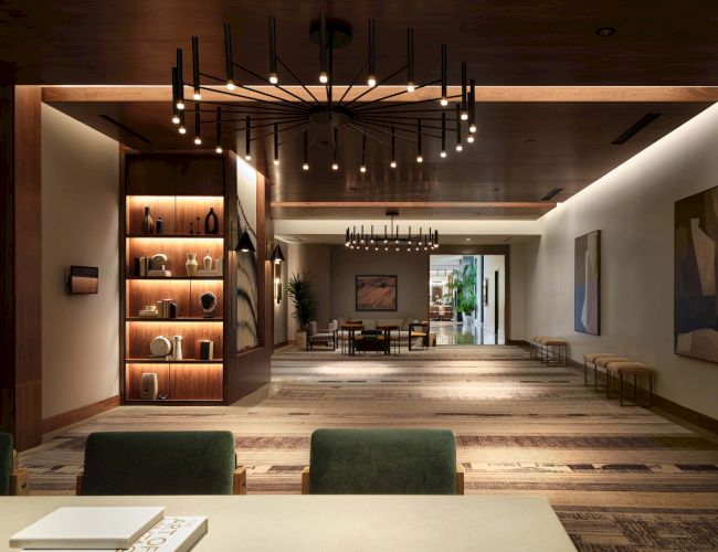 A modern lobby or lounge with warm wood accents, a long hallway, shelves lit with decor, and seating areas under contemporary lighting.
