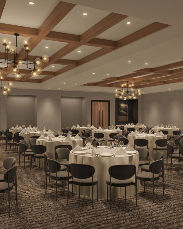A banquet hall with round tables, white tablecloths, and black chairs; chandeliers hang from the ceiling, and artwork adorns the walls.