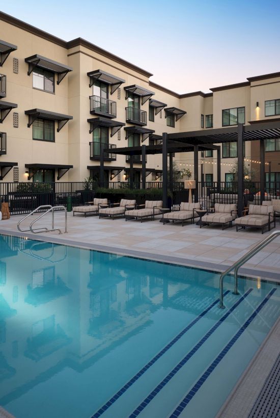 A hotel-style pool area with lounge chairs, a clear blue pool, and a multi-story courtyard building surrounding it.