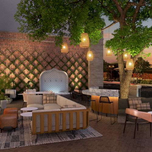 An outdoor patio with lounge seating, hanging lights, a fireplace, and a tree, creating a cozy and inviting atmosphere at sunset.
