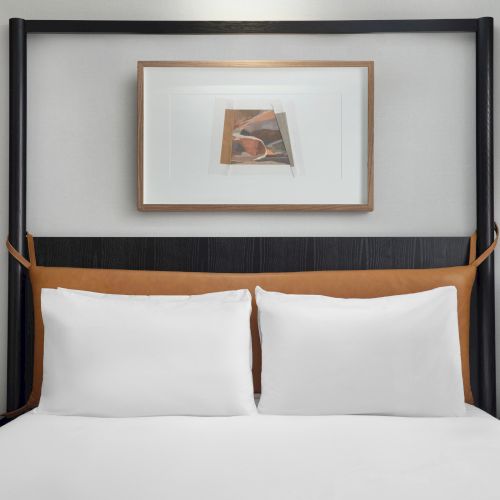 A modern bedroom with a neatly made bed, two pillows, bedside lamps, and abstract artwork above the headboard on the wall.