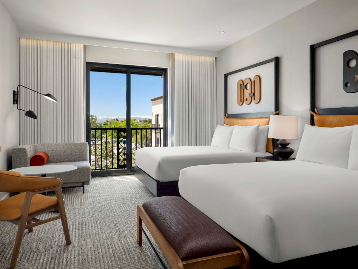 The image shows a modern hotel room with two beds, a sitting area, balcony, and stylish decor, offering a comfortable, elegant atmosphere.