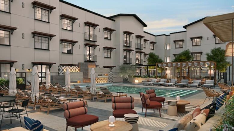 This image shows a hotel courtyard with a swimming pool, surrounded by seating, umbrellas, and a building with multiple windows.
