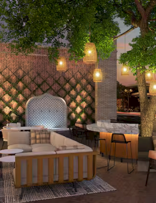 A cozy outdoor patio with seating, a fireplace, hanging lights, and a tree at sunset, creating a warm and inviting atmosphere.