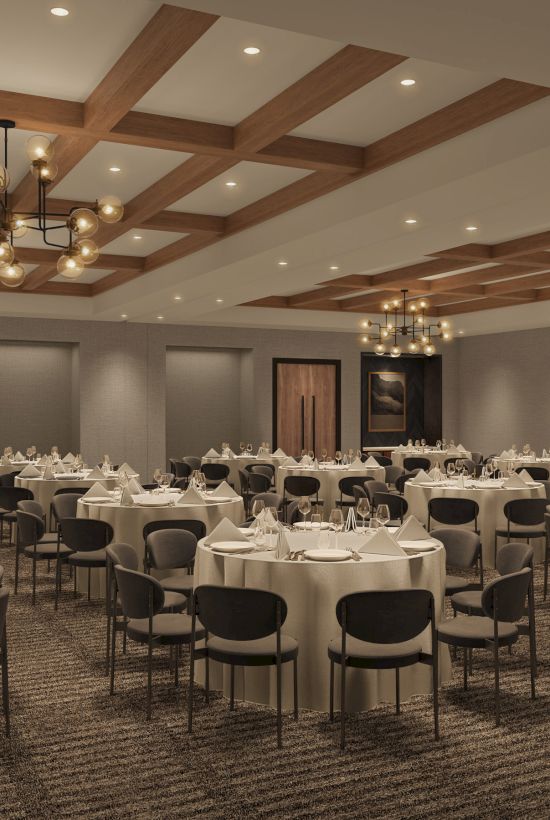 The image shows an elegant banquet hall with round tables set for dining, featuring chandeliers and a wooden coffered ceiling.