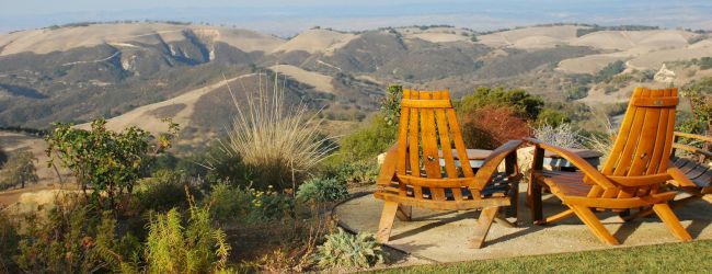 A scenic landscape with two wooden chairs overlooking rolling hills and a clear sky in the background.