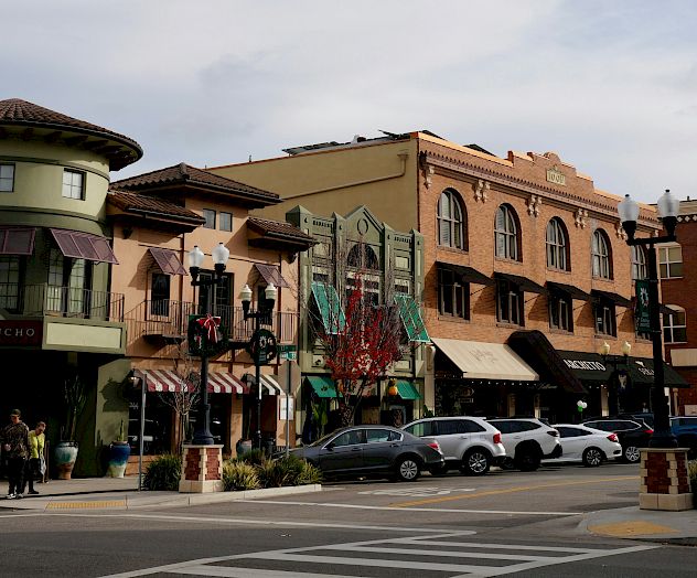 The image shows a street corner with parked cars, people, and several quaint buildings with awnings in a small-town setting.
