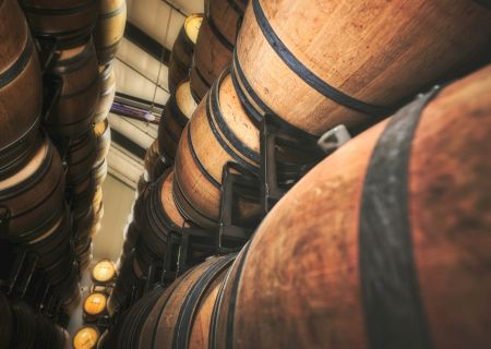 The image shows stacks of wooden barrels, likely used for aging wine or spirits, arranged in a warehouse setting.