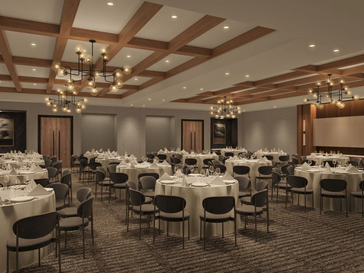 The image shows an elegant banquet hall with round tables set for an event, featuring chandeliers and wood-paneled ceilings.