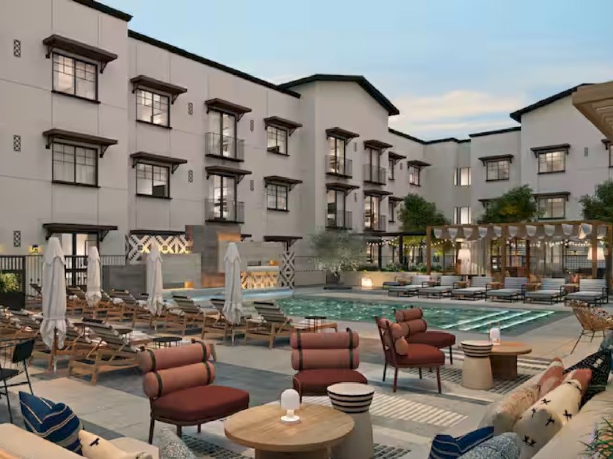 A modern hotel courtyard with a central swimming pool, surrounded by lounge chairs, tables, and greenery, offering a relaxing outdoor space.