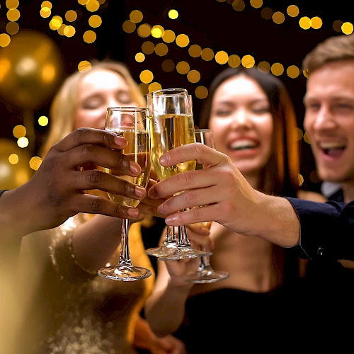 A group of people celebrating, clinking glasses, with festive lights in the background.