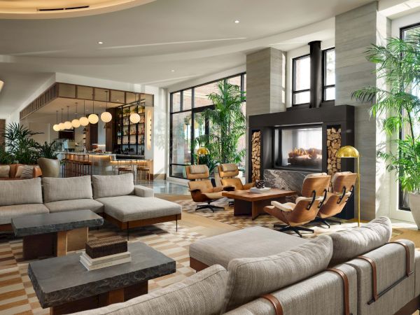 A luxe, open-plan living room with neutral sofas, wooden coffee tables, tall plants, and a cozy seating area by a modern fireplace; bright, airy, stylish.