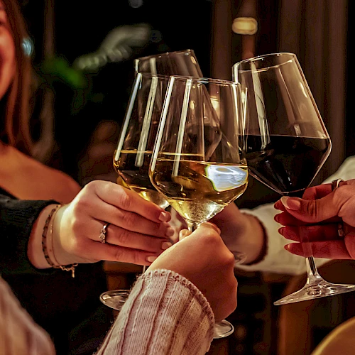 A group of people clinking wine glasses in a cheerful toast at a social gathering, with a smiling woman in the background.