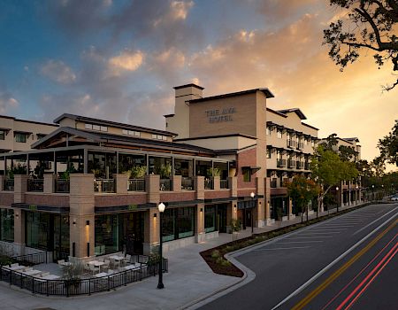 A hotel building named “The Ava” at sunset, with balconies, outdoor seating, and a quiet road lined with trees.