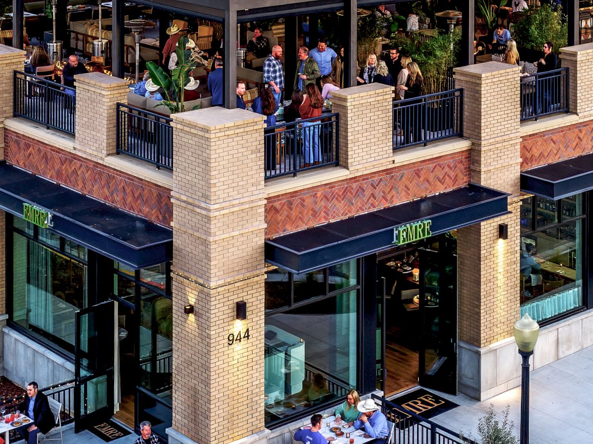 A hotel courtyard restaurant patio with people dining under an awning, with Empire signage on storefronts and doors.