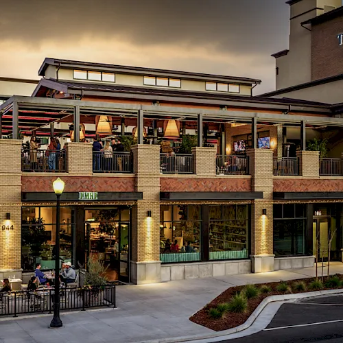 Evening view of The AVA Hotel with a brick facade, lit entrance, and an outdoor patio where people are dining.