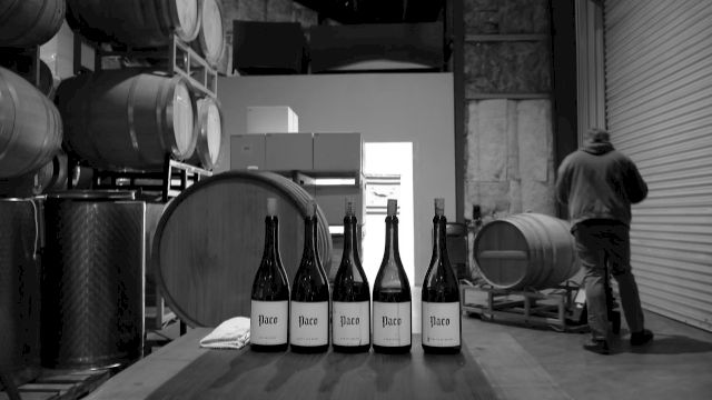 Inside a winery cellar, barrels and large drums line the room as a worker walks past a row of wine bottles labeled &ldquo;Paco&rdquo;.