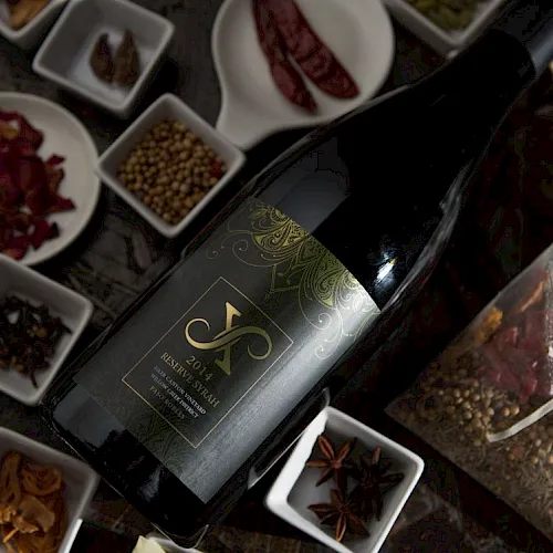 A wine bottle lies amid assorted spice bowls—peppercorns, dried chilies, and star anise.