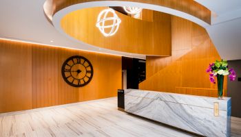 A modern lobby with a marble reception desk, wood accents, a large wall clock, and decorative lighting fixtures.