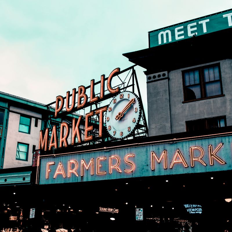 The image shows the iconic neon signs for "Public Market" and "Farmers Market" at a famous market building, with a clock in between.