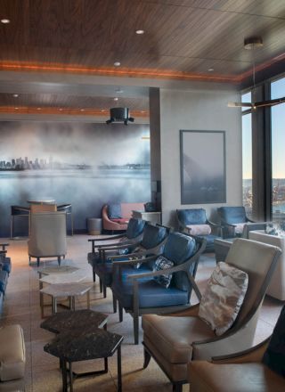 A modern lounge with plush seating, large windows offering a city and water view, and a wall mural, creating a cozy and scenic atmosphere.