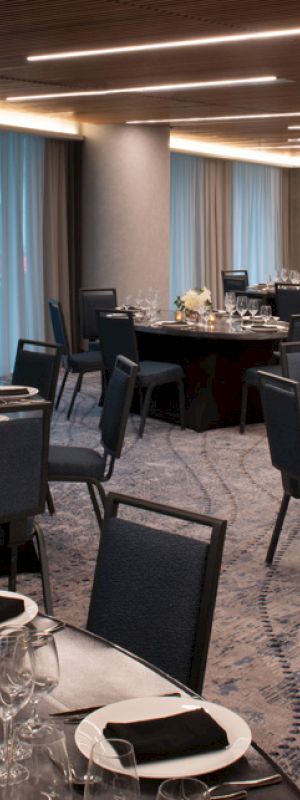 The image shows an elegantly set dining area with round tables, chairs, dim lighting, and decorative elements like flowers and candles.