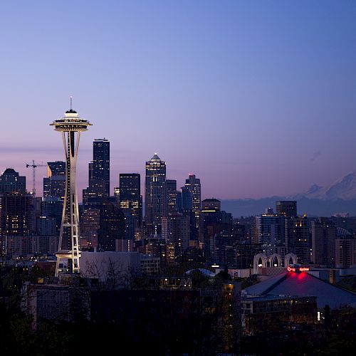 The image shows the Seattle skyline at dusk, featuring the Space Needle and city buildings with a mountain in the background.