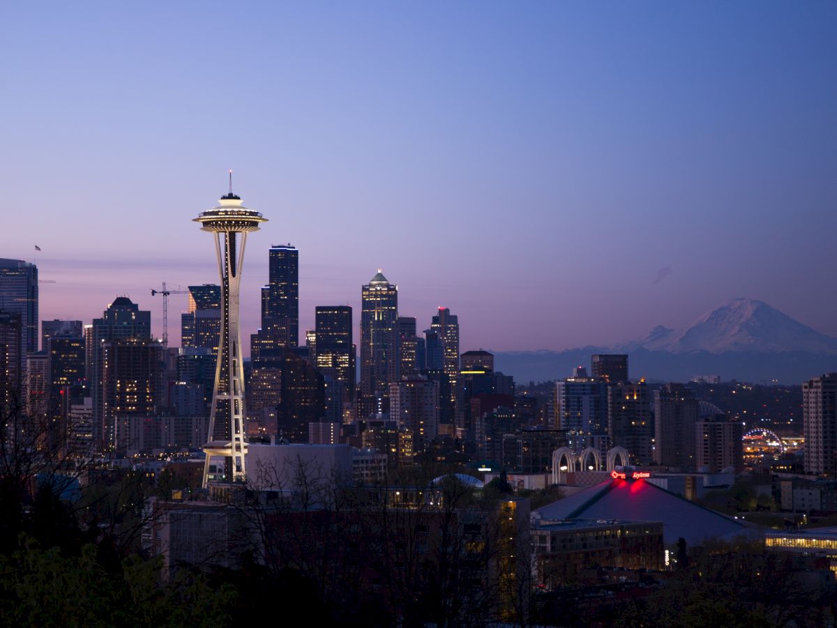 Seattle skyline at dusk with the Space Needle, surrounding buildings, and Mount Rainier visible in the backdrop.