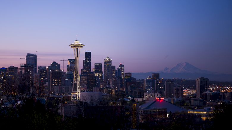 Seattle skyline at dusk with the Space Needle, surrounding buildings, and Mount Rainier visible in the backdrop.
